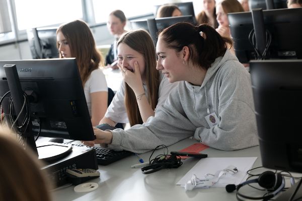 Schülerinnen reden und arbeiten vorm Computer