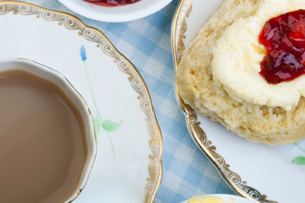 Britische Teezeit. Eine Tasse mit Tee und ein Teller mit Scones mit Erdbeermarmelade.