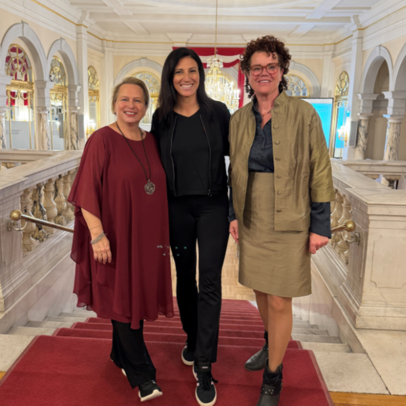 Drei Frauen stehen vor einer Treppe mit rotem Teppich.
