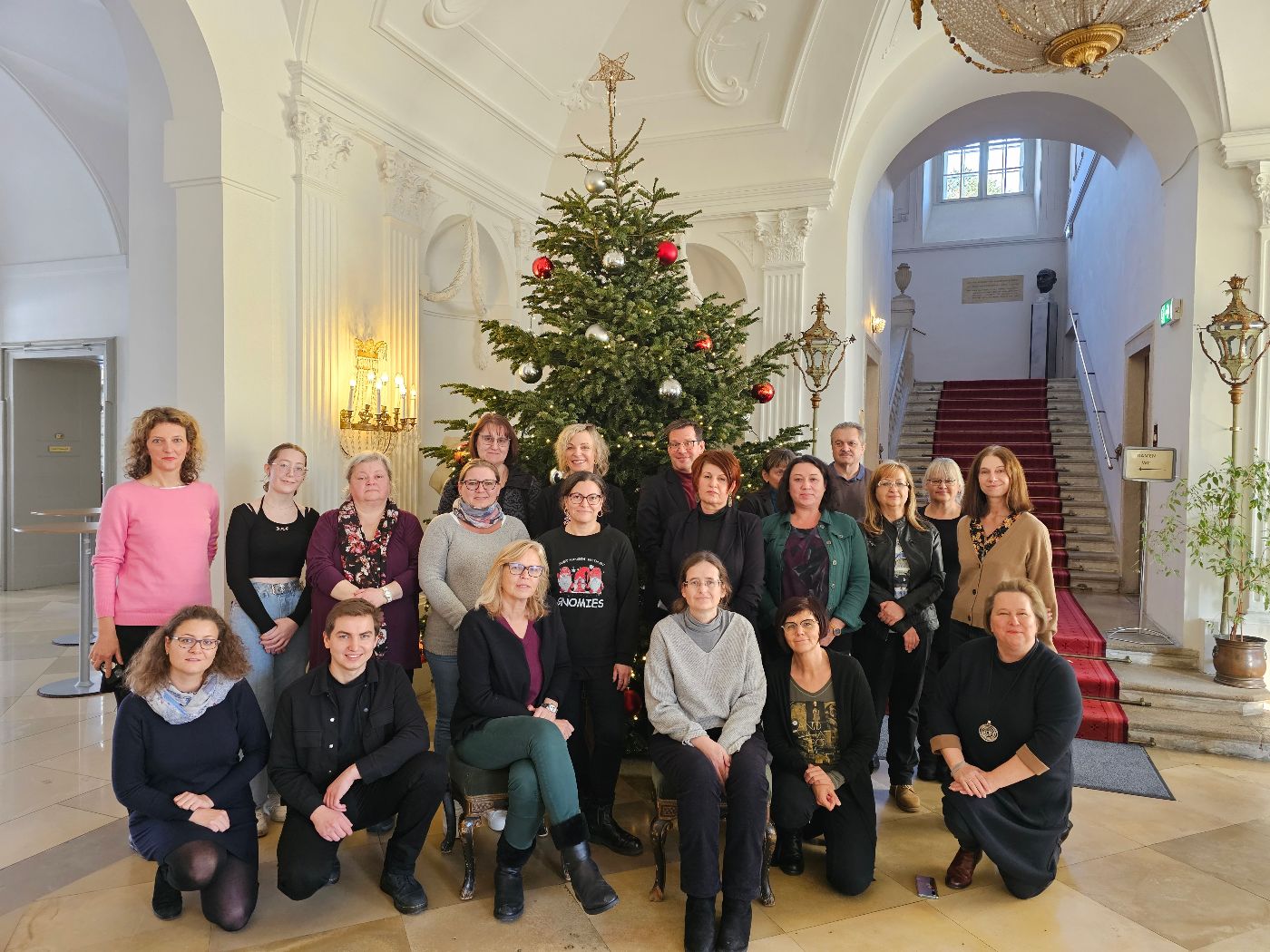 Das Team der Abteilung Verwaltungsakademie. 22 Personen stehen und sitzen vor einem großen Weihnachtbaum im Schloss Laudon.