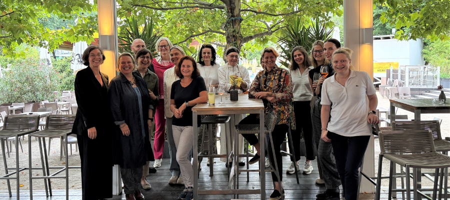 Eine Gruppe Frauen steht für ein Gruppenfoto zusammen. Im Hintergrund sind Stühle und Tische.