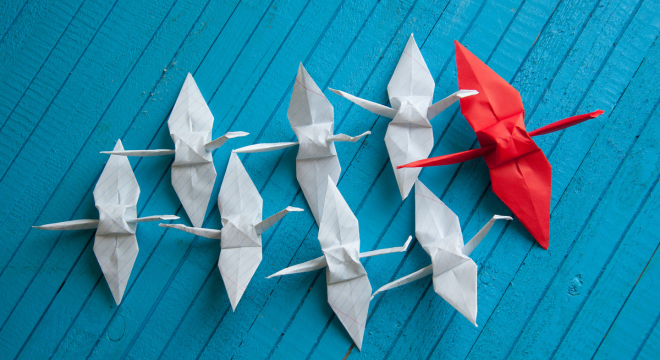 Weiße Origami Kraniche folgen einem roten Origami Kranich. Der Hintergrund ist blau.